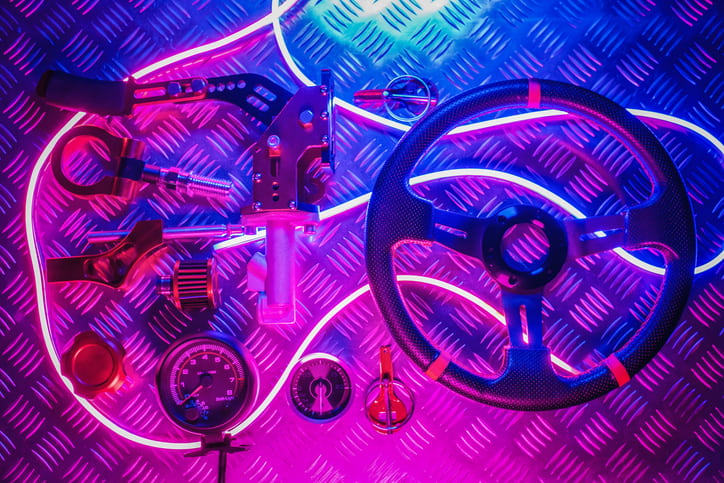 Steering wheel and other automobile pieces on a metal plate with blue and purple neon lights around them
